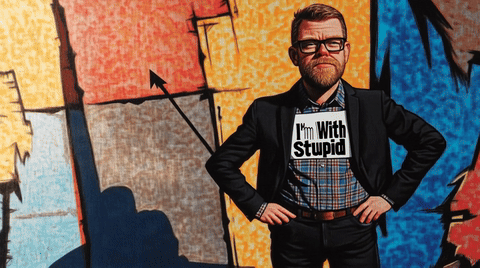 Man wearing glasses and a suit with a sign that says 'I'm With Stupid' on a colorful wall.