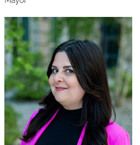 Portrait of Jim Paine, the Mayor, wearing a pink suit and black top, with long dark hair.
